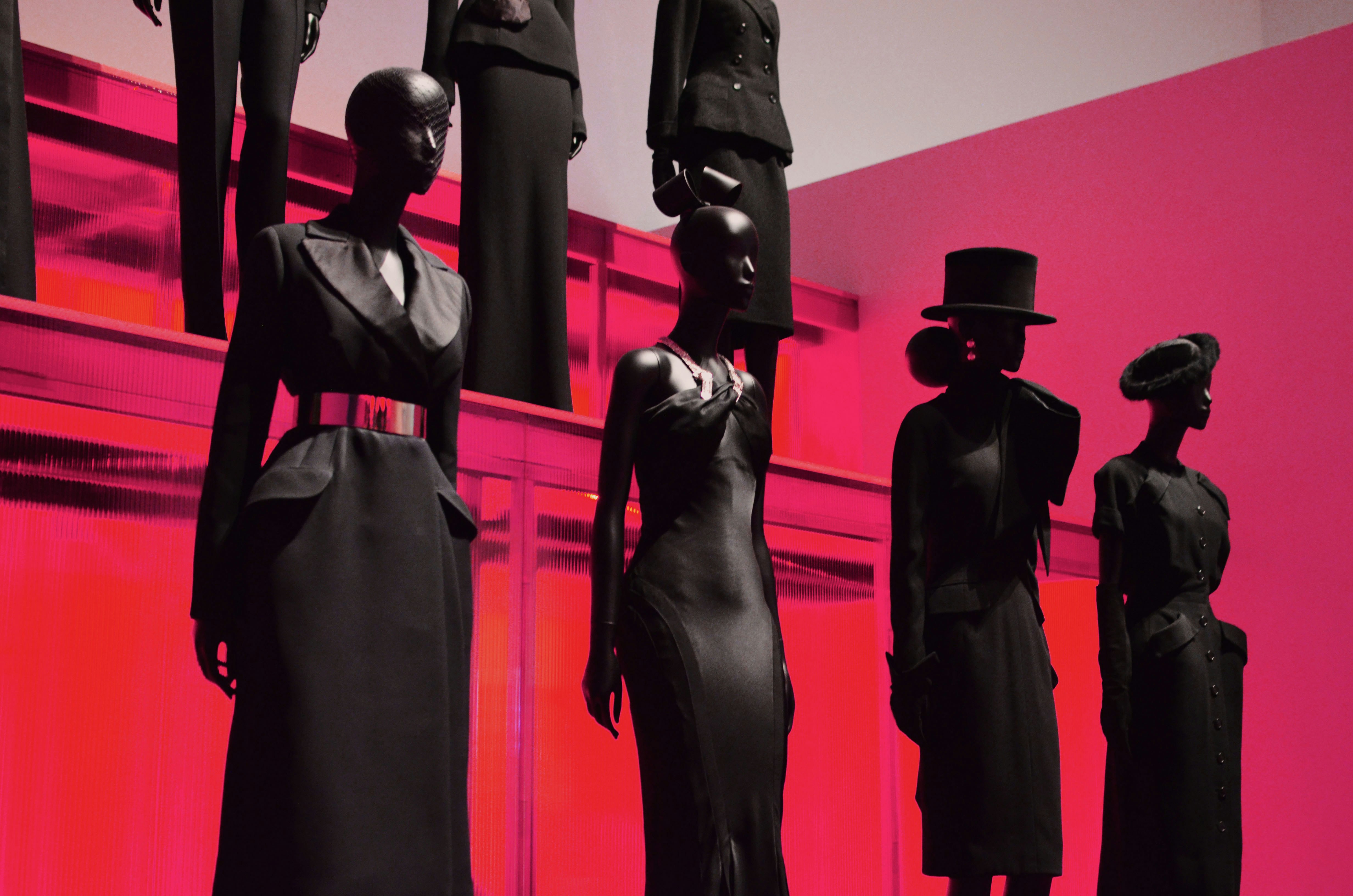 four black mannequins in black attires standing in a red room